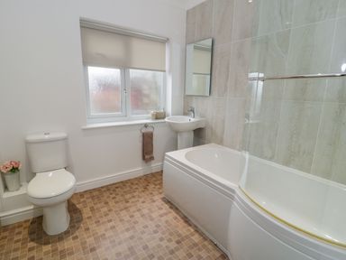 A bathroom with a toilet, pedestal sink, bathtub with glass shower screen, tiled wall and window at Hendre Wylan in Llanaber