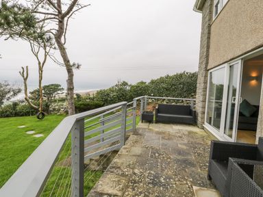 A patio with outdoor furniture and a grassy area with a tree and a tire swing at Hendre Wylan in Llanaber