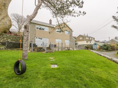 A house with a grass lawn and a tire swing hanging from a tree at Hendre Wylan in Llanaber