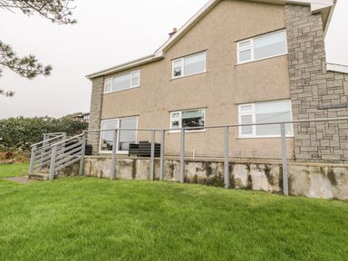 Exterior view of a two story house with multiple windows a small outdoor seating area stairs and a grassy lawn at Hendre Wylan in Llanaber