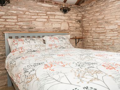 A bedroom with a bed covered in white bedding with a berry pattern and stone walls at The Cow Cott in Hereford