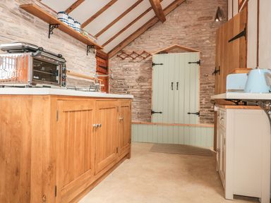 A kitchen with wooden cabinets a toaster oven a blue kettle and toaster and stone walls at The Cow Cott in Hereford