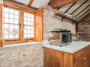 A kitchen with a dualit toaster oven on a wooden counter near a window with wooden shutters at The Cow Cott in Hereford