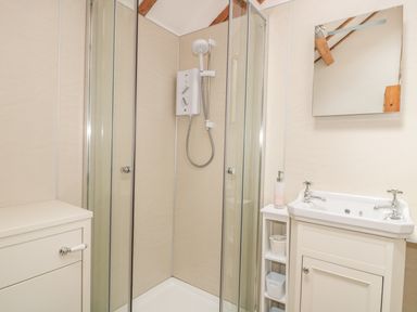 A bathroom with a corner shower enclosure a sink with a mirror above and a small cabinet with shelves at The Cow Cott in Hereford