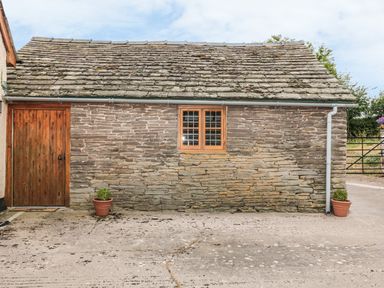 A stone building with a wooden door and window and two potted plants at The Cow Cott in Hereford