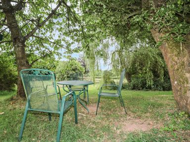 An outdoor seating area with metal table and chairs under trees in a garden at The Cow Cott in Hereford