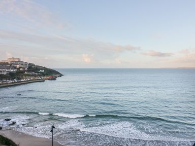 A coastal view of a beach with waves and houses on a hillside near the shore at Onshore 6 - Newquay Towan Beach View in Newquay