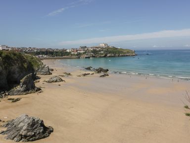 A sandy beach with rocks and people near the shoreline with houses and cliffs in the background at Onshore 6 - Newquay Towan Beach View in Newquay