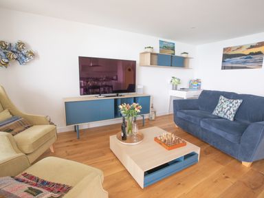A living room with blue and beige furniture a tv on a blue and wooden stand and a coffee table with flowers and chess at Onshore 6 - Newquay Towan Beach View in Newquay