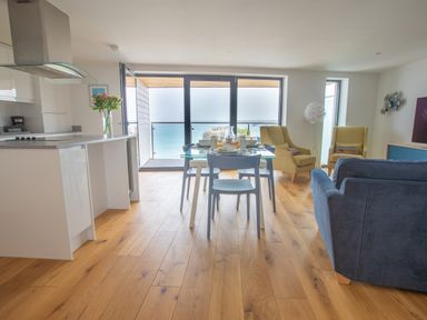 A kitchen and dining area with a glass table and blue chairs overlooking the sea at Onshore 6 - Newquay Towan Beach View in Newquay