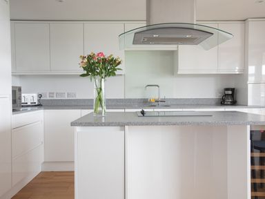 A kitchen with white cabinets a granite countertop a stove hood a vase with flowers and kitchen appliances at Onshore 6 - Newquay Towan Beach View in Newquay