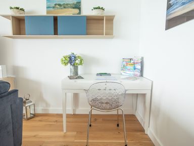 A white desk with a transparent chair and flower vase on wood floor at Onshore 6 Newquay Towan Beach View in Newquay