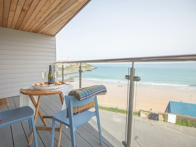A balcony with a wooden table set with food and drinks and blue chairs overlooking a beach at Onshore 6 - Newquay Towan Beach View in Newquay