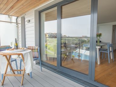 A balcony with a small table set with a bottle, glasses, and snacks next to blue chairs with plaid blankets at Onshore 6 - Newquay Towan Beach View in Newquay