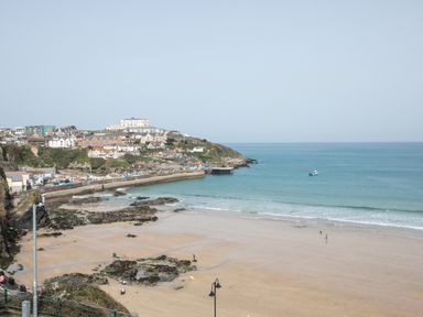 A beach with sand and rocks next to a coastal town and a small boat in the water at Onshore 6 - Newquay Towan Beach View in Newquay