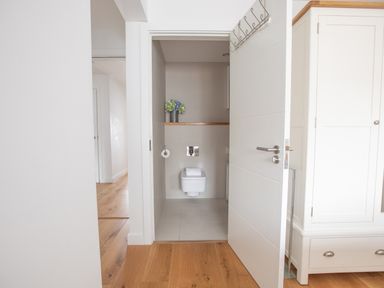 A view into a small bathroom with a wall-mounted toilet and a shelf with vases of flowers at Onshore 6 - Newquay Towan Beach View in Newquay