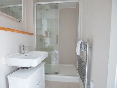 A bathroom with a sink, a glass shower enclosure, and a heated towel rail with a towel at Onshore 6 - Newquay Towan Beach View in Newquay
