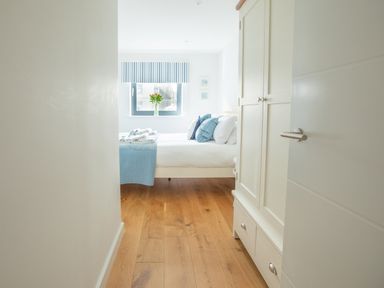 A bedroom with a bed, pillows, towels, a wardrobe, a window with striped blinds and a vase of flowers at Onshore 6 - Newquay Towan Beach View in Newquay