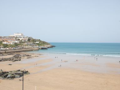 A beach with people walking and swimming near the ocean and houses on a hill in the background at Onshore 6 - Newquay Towan Beach View in Newquay