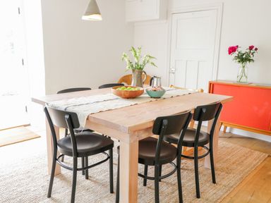 A dining room with a wooden table and black chairs a sideboard with flowers and a door at Whitehall Farm Cottage in Honiton