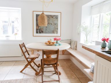 A kitchen dining area with a round wooden table two wooden chairs a built in bench with cushions and flowers in vases at Whitehall Farm Cottage in Honiton