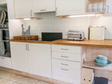 A kitchen counter with a toaster cutting board and bowls on shelves at Whitehall Farm Cottage in Honiton
