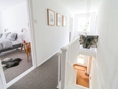A hallway with framed pictures on the wall a bedroom doorway to the left and stairs leading down at Whitehall Farm Cottage in Honiton