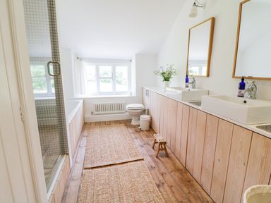 A bathroom with two sinks and mirrors a toilet a bathtub wooden flooring and rugs at Whitehall Farm Cottage in Honiton