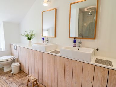 A bathroom with two sinks two mirrors a toilet wooden cabinets and a small wooden stool at Whitehall Farm Cottage in Honiton