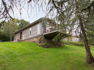 A wooden house with a stone base on a grassy hill surrounded by trees at 6 Lake View in Lanreath