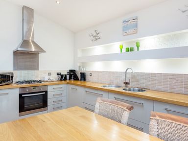 A kitchen with wooden countertops gray cabinets a gas stove double sink and a wooden table at 6 Lake View in Lanreath