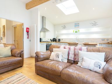 A living room with brown leather sofas and cushions next to a kitchen with a skylight at 6 Lake View in Lanreath