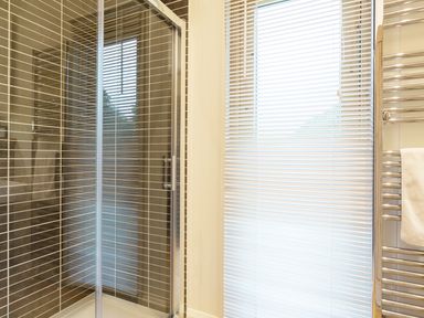 A shower enclosure with glass doors and a window with blinds next to a towel rack in a bathroom at 6 Lake View in Lanreath