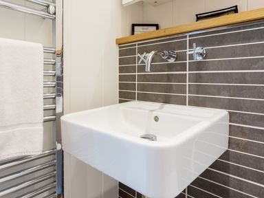 A bathroom sink with a wall-mounted faucet and controls next to a chrome towel rack with a white towel at 6 Lake View in Lanreath