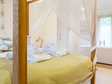 A bedroom with a four-poster bed covered with a green blanket and white robes on the bed at 6 Lake View in Lanreath