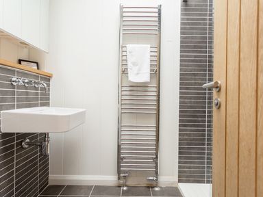 A bathroom with a wall-mounted sink a chrome towel radiator with a white towel and a wooden door at 6 Lake View in Lanreath