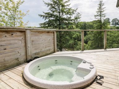 A wooden deck with a round hot tub overlooking trees at 6 Lake View in Lanreath