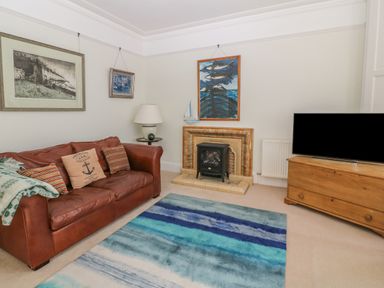 A living room with a brown leather sofa a blue striped rug a small fireplace a wooden TV stand with a television and framed pictures on walls at 11 Marine Terrace in Criccieth
