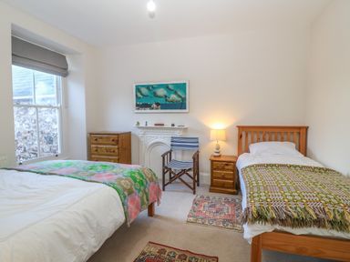 A bedroom with two single beds wooden furniture a painted wall fireplace window and patterned rugs at 11 Marine Terrace in Criccieth
