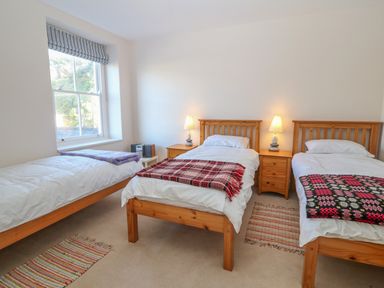 A bedroom with three single beds wooden headboards bedside tables with lamps and a window at 11 Marine Terrace in Criccieth