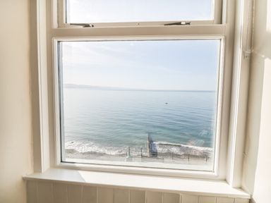 A window with a view of the sea and a beach with waves at 11 Marine Terrace in Criccieth
