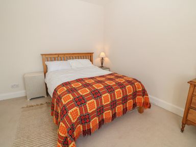 A bedroom with a wooden bed with a colorful blanket a lamp on a bedside table and a wooden dresser at 11 Marine Terrace in Criccieth