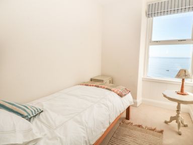 A bedroom with a single bed next to a window overlooking the sea at 11 Marine Terrace in Criccieth