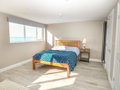 A bedroom with a wooden bed and a blue blanket next to a window showing the sea at 11 Marine Terrace in Criccieth