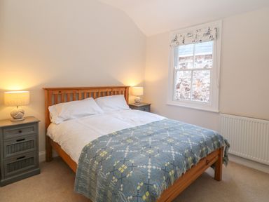 A bedroom with a wooden bed framed by two bedside tables with lamps and a window with patterned blind at 11 Marine Terrace Criccieth