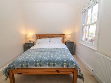 A bedroom with a wooden bed a blue patterned blanket two bedside tables with lamps and a window at 11 Marine Terrace in Criccieth
