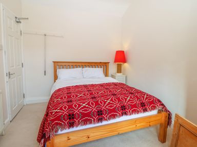 A bedroom with a wooden bed with white pillows and a red patterned blanket at 11 Marine Terrace in Criccieth