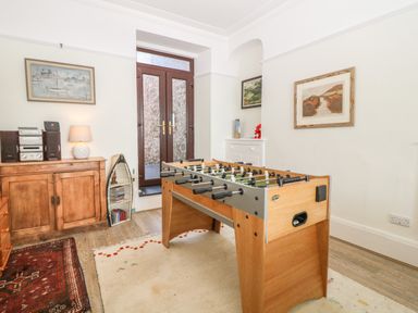 A room with a foosball table a wooden cabinet with a stereo system and a lamp and a white chest with decorations at 11 Marine Terrace in Criccieth