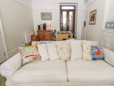 A room with a white sofa with cushions a foosball table wooden furniture and double doors at 11 Marine Terrace in Criccieth