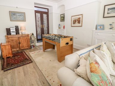A living room with a foosball table wooden cabinets and a sofa with pillows at 11 Marine Terrace in Criccieth